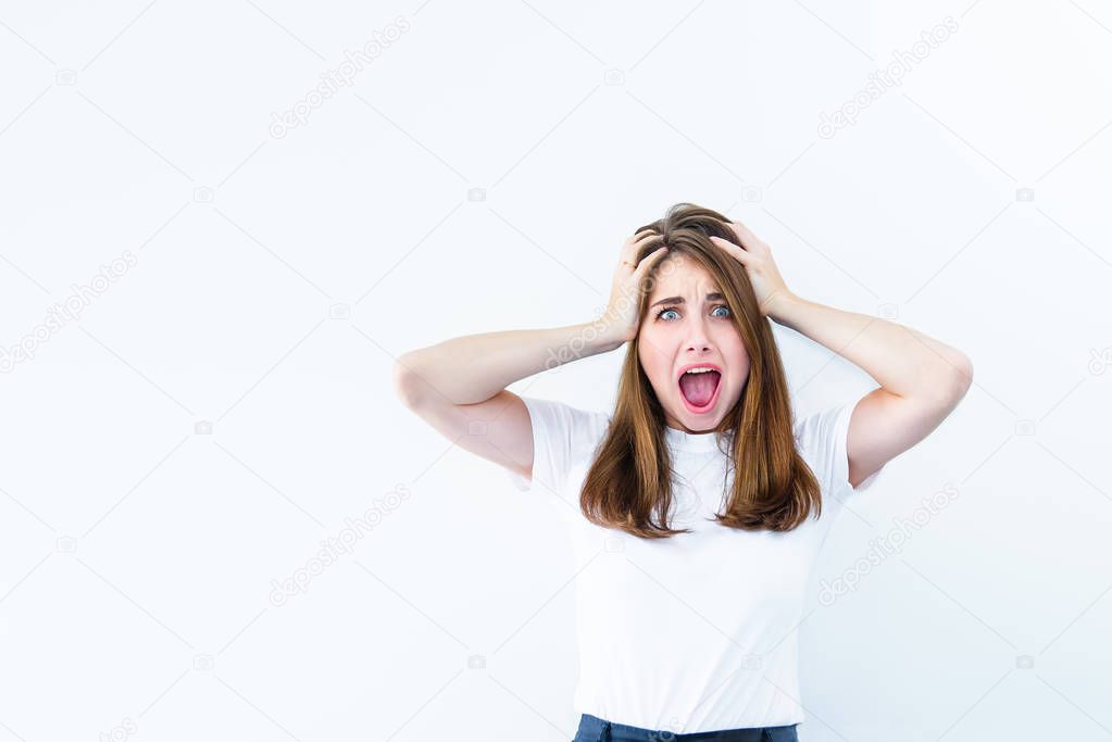 Horrible, stress, shock. Young emotional suprised woman looks at camera, clasping head in hands and opening her mouth isolated on white background. Human emotion, facial expression concept. Copy space.