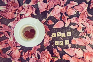 Flatlay fincan kahve kalp şekli desen ve seni seviyorum mesaj ile pembe peony çiçek yaprakları koyu arka plan üzerinde ahşap bloklar yazıldığından. Sevgililer günü, Günaydın kavramı. Vintage. Üstten görünüm.