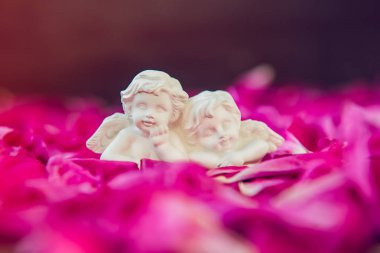 İki antika küçük güzel melekler pembe mor peony çiçek yaprakları siyah taş zemin üzerine alçı heykelciği. Aşk, Romantik, Sevgililer günü kavramı. Yakın, yumuşak seçici odak.
