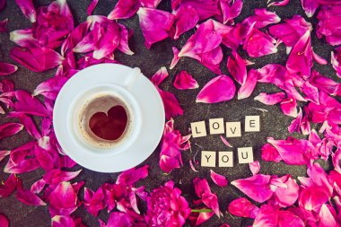 Düz yatıyordu fincan kahve kalp şekli desen ve seni seviyorum mesaj ile mor pembe peony çiçek yaprakları siyah arka plan üzerine ahşap bloklar yazıldığından. Sevgililer günü, Günaydın kavramı. Üstten görünüm.
