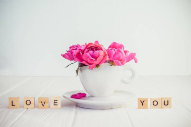 Hafif pembe şakayık çiçekleri buketi bir dekoratif Kupası ve fincan tabağı ve seni seviyorum mesaj yakın Beyaz ahşap zemin üzerinde ahşap bloklar yazıldığından. Sevgililer günü, Günaydın kavramı. Kopya alanı