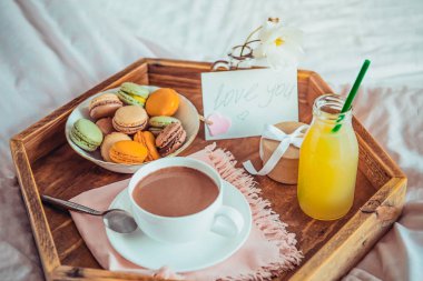 Yatakta kahvaltı ile bir not metni seviyorum. Bir fincan kahve, meyve suyu, Bademli kurabiye, gül çiçek ve giftbox ahşap tepsi. Yatakta romantik kahvaltı. Doğum günü, Sevgililer günü sabah. Kopya alanı