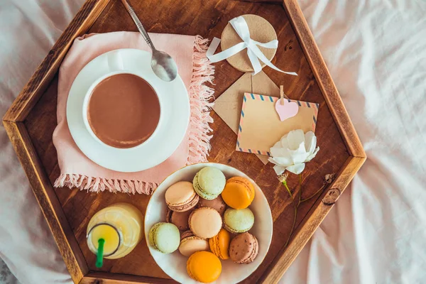 Breakfast in bed with empty blank card for text. Cup of coffee, juice, macaroons, rose flower and giftbox on wooden tray. Romantic breakfast in bed. Birthday, Valentine's day morning. Copy space — Stock Image Breakfast Bed Empty Blank Card Text Cup Coffee Juice Macaroons Royalty Free Stock Photos