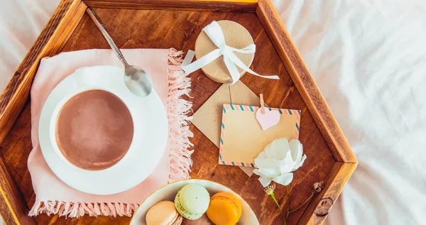 Breakfast in bed with empty blank card for text. Cup of coffee, juice, macaroons, rose flower and giftbox on wooden tray. Romantic breakfast in bed. Birthday, Valentine's day morning. Copy space — Stock Image Breakfast Bed Empty Blank Card Text Cup Coffee Juice Macaroons Royalty Free Stock Photos