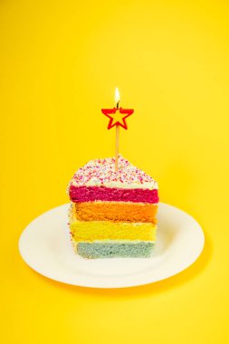 Birning mum parlak sarı arka plan üzerinde izole beyaz yuvarlak plaka üzerinde yıldız şeklinde Gökkuşağı pasta dilimi. Mutlu yıllar, parti kavramı. Dikey kart. Seçici odak. Kopya alanı
