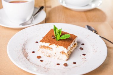 Kahve çekirdekleri ve açık ahşap renkli bir tabağa üzerinde taze nane ile leziz Tiramisu pasta. Seçici odak, kopya alanı