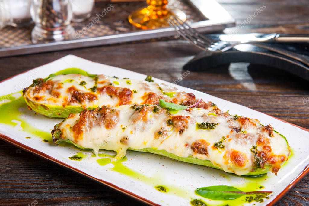 Close up Baked stuffed zucchini boats. Zucchini stuffed with meat and cheese and pesto sauce served on the white plate on the dark wooden table. Healthy food concept