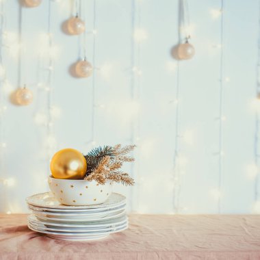 Noel tablosu ayarı. Duvar üzerinde bulanık ışıklar ve topları ile bej masa örtüsü üzerinde altın dekor ve köknar ağacı ile beyaz yemekler servis edilmez. Şenlikli arka plan. Meydanı. Yumuşak seçici odaklama. Boşluk Kopyala.