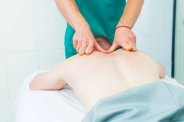 Patient receiving massage from therapist. A chiropractor does deep tissue massage on man's shoulder blade in medical office. Neurological physical examination. Osteopathy, chiropractic, physiotherapy.