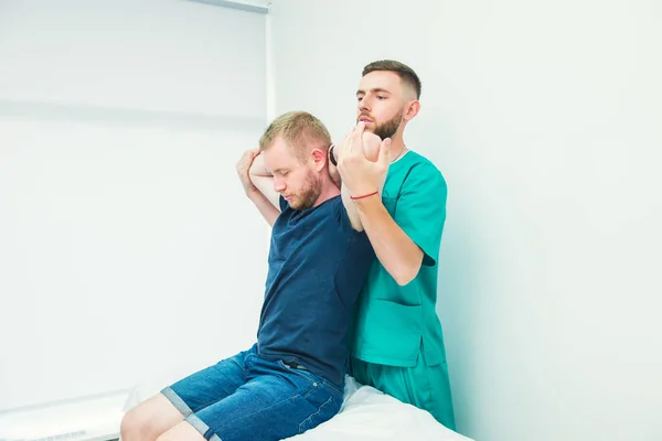 Paciente do sexo masculino recebendo massagem do terapeuta. Um quiroprático a esticar a coluna e as mãos do paciente no consultório médico. Exame físico neurológico. Osteopatia, quiropraxia, fisioterapia . — Fotografia de Stock
