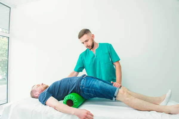 Homem na fisioterapia fazendo exercícios físicos com seu terapeuta, eles usam um rolo de massagem. Um quiroprático trata a coluna vertebral dos lombos do paciente em consultório médico. Neurologia, Osteopatia, quiropraxia . — Fotografia de Stock