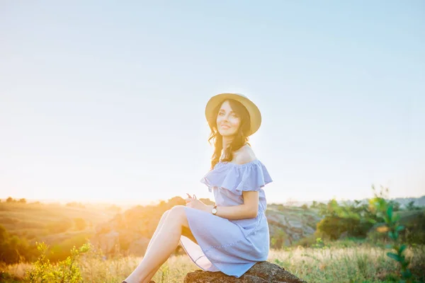 Retrato de jovem mulher em vestido romântico azul e chapéu de palha na luz do sol desfrutando do pôr do sol de verão na natureza. Calma e harmonia. Férias de verão, diversão, humor positivo. Luz solar de volta, raios de sol. Espaço de cópia . — Fotografia de Stock