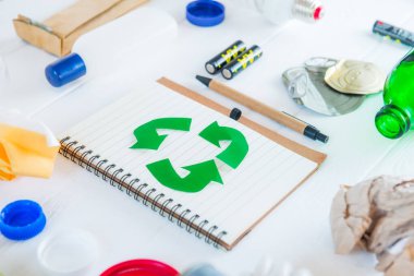 Yeşil eko sembolü ile geri dönüşüm olmayan çöp ve metal, plastik, eski kağıt, beyaz ahşap arka plan üzerinde cam ürünleri gibi yeniden kullanılabilir atık ile çevrili kağıt defter geri dönüşüm. Seçici odaklama.