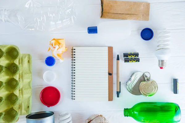 Recycling und Nicht-Recycling-Müll und wiederverwendbare Abfallwirtschaft als Metall, Kunststoff, Altpapier, wiederverwendbare Glasprodukte und leeres Notizbuch auf weißem Holzgrund. Kopierraum. — Stockfoto