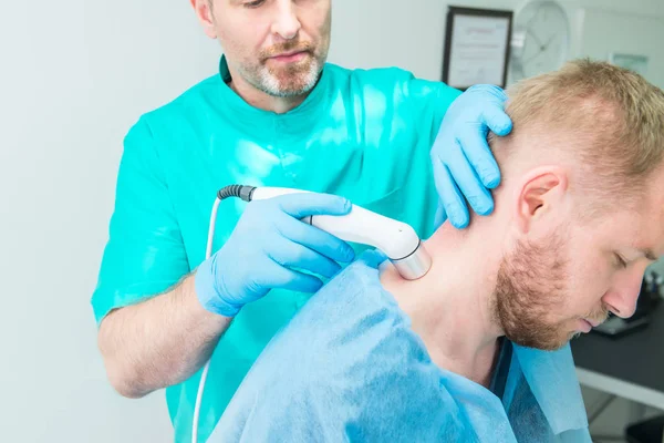 Junger Mann in der Physiotherapie bei einer Lasertherapie-Massage. Ein Chiropraktiker behandelt die Halswirbelsäule des Patienten in der Arztpraxis. Neurologie, Osteopathie, Chiropraktik. Selektiver Fokus, Kopierraum. — Stockfoto