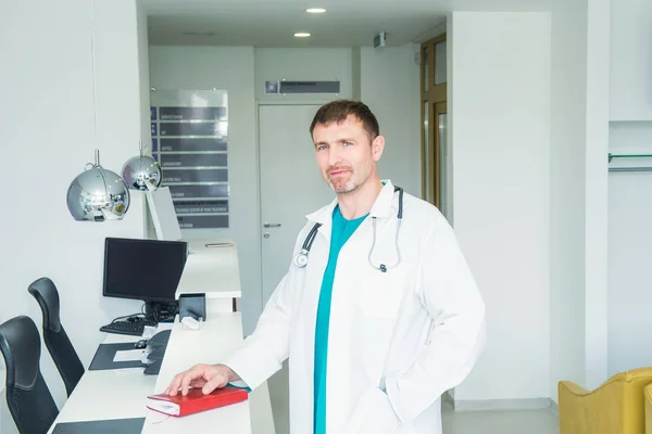 Volwassen man zelfverzekerd Doctor's portret staande op ziekenhuis receptiebalie in de hal van de moderne medische kliniek. Gezondheidszorg en mrdicine-concept. Selectieve focus, kopieer ruimte. — Stockfoto