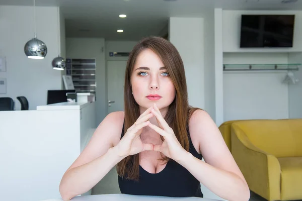 Retrato de cerca de una joven mujer seria y segura de sí misma con un decolete profundo, mirando a la cámara, sosteniendo la mano cerca de la cara, mirando seriamente sobre el fondo de un pasillo de oficinas. Copiar espacio . —  Fotos de Stock