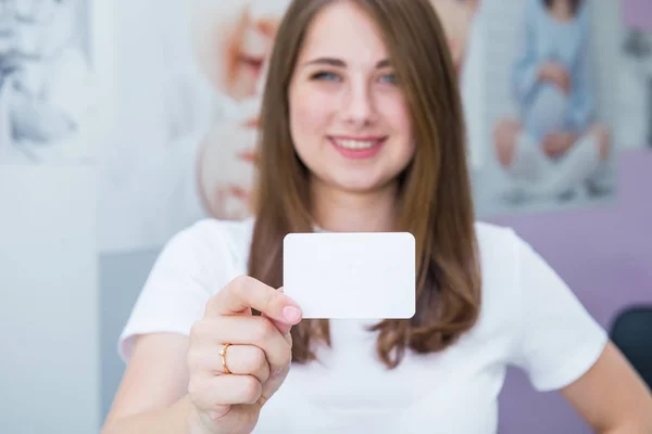 명함 또는 기프트 카드. 흐릿한 행복하고 흥분 백인 여성은 가벼운 실내 배경에 디자인을위한 복사 공간이 집중 빈 빈 종이 카드를 보여주는 캐주얼 옷을 입고. — 스톡 사진