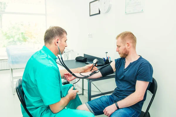 Erkek Doktor hastanede genç bir erkek hastaya kan basıncı kontrol stetoskop ile sphygmomanometer kullanarak. Sağlık, sağlıklı yaşam tarzı ve tıbbi hizmet kavramı. Kopyalama alanı. — Stok fotoğraf