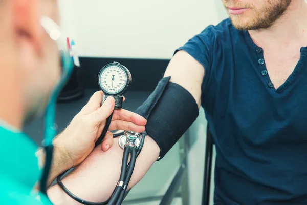 Close up Male Doctor using sphygmomanometer with stethoscope checking blood pressure to a young male patient in the hospital. Healthcare, healthy lifestyle and medical service concept. Copy space. — Stock Photo, Image