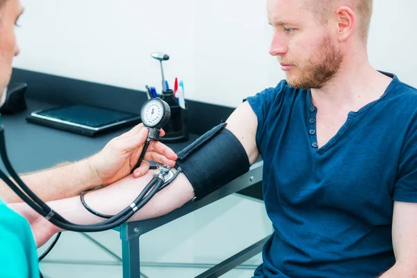 Чоловік Доктор використовує склерометр зі стетоскопом для перевірки артеріального тиску молодого пацієнта в лікарні. Здоров'я, здоровий спосіб життя та концепція медичного обслуговування. Копіювати простір . — стокове фото