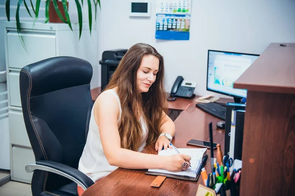 Young caucasian business lady sitting on her workplace in office. Female entrepreneurship. Portrait of skilled manager satisfied with occupation. Selective focus, copy space. — Stock Photo, Image