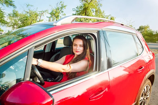 笑顔のビジネス女性の肖像画、赤い服を着た白人の若い女性ドライバーがカメラを見て、車輪の赤い車の後ろに座っている間に微笑んでいます。選択的な焦点、コピースペース. — ストック写真