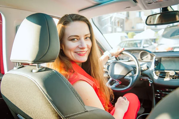 バックビュー 笑顔のビジネスレディ、白人の若い女性ドライバーがカメラを見て、車を運転しながら彼女の肩の上に微笑む。選択的な焦点、コピースペース。内側のビュー. — ストック写真