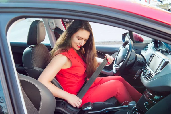 ビジネスレディの肖像画、赤い夏のスーツを着た白人の若い女性ドライバーは、車輪の後ろに座っている間、車のシートベルトを締めます。安全運転コンセプト。選択的な焦点、コピースペース. — ストック写真