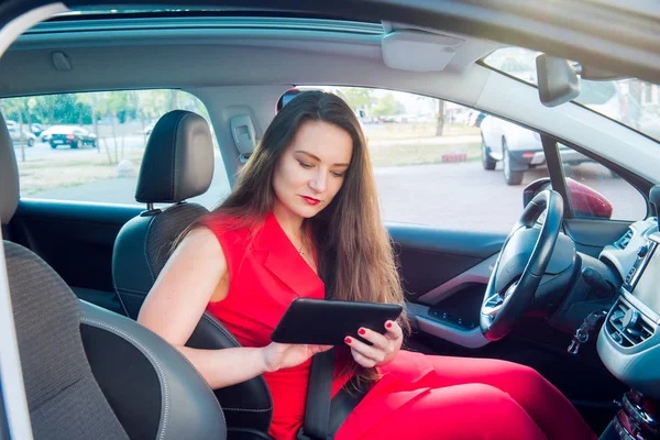 真面目なビジネスレディの肖像画、赤い夏のスーツを着た白人の若い女性ドライバーは、車輪の後ろに座っている間、ナビゲーターにルートを設定します。側面図。選択的な焦点、コピースペース. — ストック写真