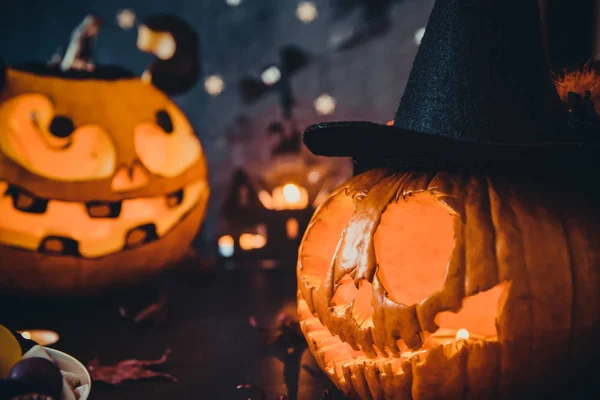 Close up Two Carved luminous pumpkins with scary evil faces, burning candles and paper silhouettes of bats, castle, ghosts on black stone background. Spooky holiday symbols and celebration concept.