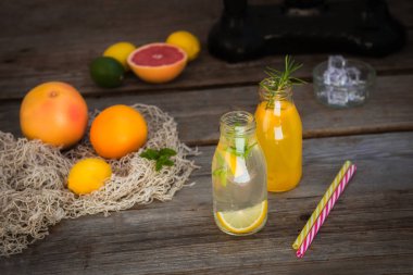 Vintage ölçekte taze narenciye ve etrafında bazı friuts ile rustik ahşap arka plan üzerinde nane ve buz ile ev yapımı limonata ve portakal taze suyu ile iki şişe. Sağlıklı Yaz içecekleri.