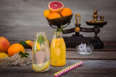 Vintage ölçekte taze narenciye ve etrafında bazı friuts ile rustik ahşap arka plan üzerinde nane ve buz ile ev yapımı limonata ve portakal taze suyu ile iki şişe. Sağlıklı Yaz içecekleri.