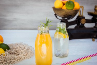 Vintage ölçekte taze narenciye ve etrafında bazı friuts ile beyaz ahşap arka plan üzerinde nane ve buz ile ev yapımı limonata ve portakal taze suyu ile iki şişe. Sağlıklı Yaz içecekleri.