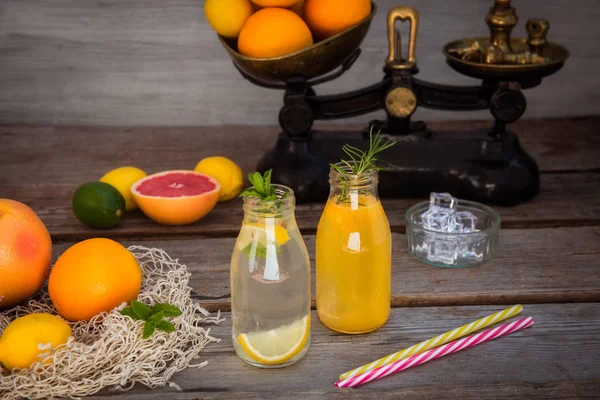 Två flaskor med hemlagad lemonad och apelsinjuice med mynta och is på den rustika trä bakgrunden med fräsch citrus i vin Tage skala och några Friuts runt om. Hälsosamma sommar drinkar. — Stockfoto