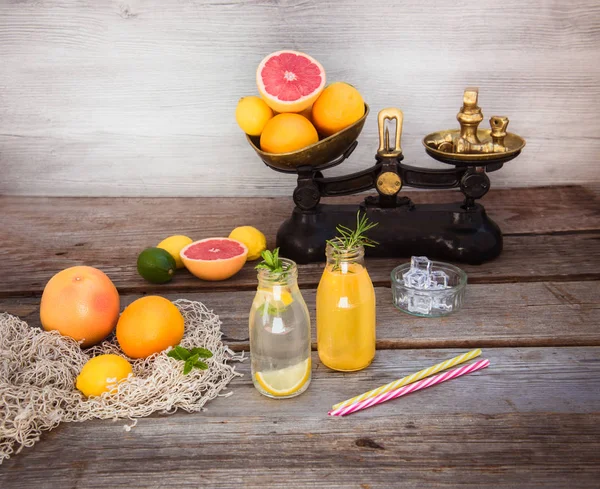 Två flaskor med hemlagad lemonad och apelsinjuice med mynta och is på den rustika trä bakgrunden med fräsch citrus i vin Tage skala och några Friuts runt om. Hälsosamma sommar drinkar. — Stockfoto