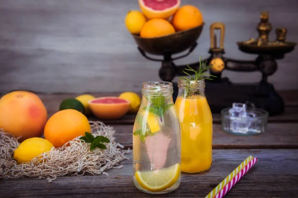 Vintage ölçekte taze narenciye ve etrafında bazı friuts ile rustik ahşap arka plan üzerinde nane ve buz ile ev yapımı limonata ve portakal taze suyu ile iki şişe. Sağlıklı Yaz içecekleri.