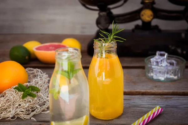 Vintage ölçekte taze narenciye ve etrafında bazı friuts ile rustik ahşap arka plan üzerinde nane ve buz ile ev yapımı limonata ve portakal taze suyu ile iki şişe. Sağlıklı Yaz içecekleri.
