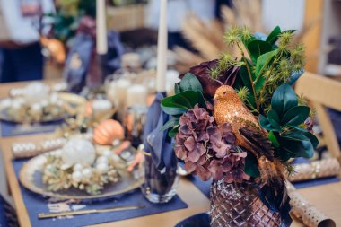 Noel sofrasında parlak kuşlu egzotik Noel buketi dekorasyonu, içinde güzel detaylar ve mavi ve altın renkli mumlar olan şenlikli yemek takımı. Donanma Mavi Masa Çarşafları ve Altın çatal bıçak.