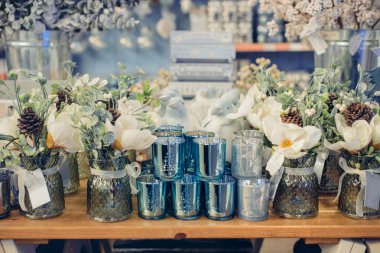 Mağazanın vitrininde gümüş, beyaz, açık mavi yılbaşı süslemeleri. Çiçekli, koni ve boncuklu şenlikli buketler. Kış Tatili Dekorasyonu. Seçici odak, boşluğu kopyala.