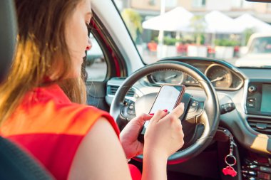 Kafkasyalı beyaz kadın sürücü dokunmatik ekranlı akıllı telefon kullanıyor ve araba sürerken mesaj yazıyor. Seçici odak, uzayı kopyala. İç görünüm.