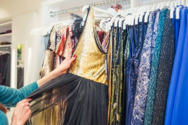 Kadın ellerini kapayarak, sergi salonundaki elbise askılarıyla etkinlik için şık bir gece elbisesi seçiyorlar. Alışveriş Merkezi 'nde. Alışverişçi. Satışlar. Alışveriş Merkezi. Seçici odak.