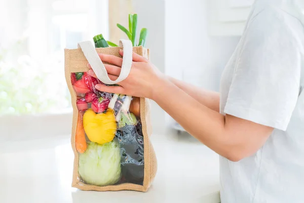 Close up female hands holding reusable bio eco sackcloth fabric bag packaging with fresh organic vegetables on white kitchen table. Home delivery concept. Local farmer healthy food. Zero waste. — Stock Photo, Image