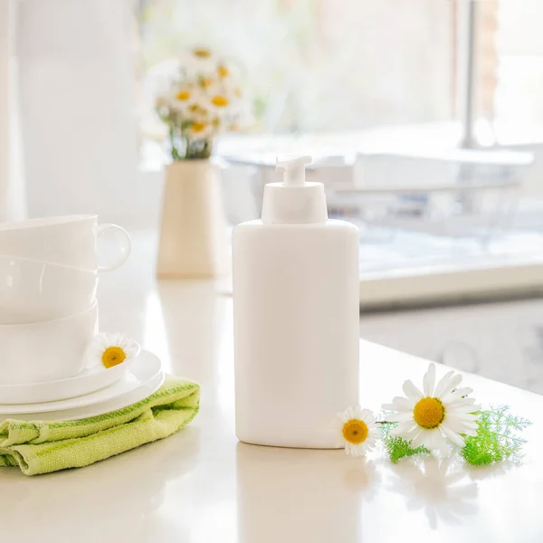 Limpiador no tóxico ecológico con ingredientes naturales, flores de manzanilla, vasos blancos limpios y platos en la mesa de la cocina blanca. Cuidado de la piel para la limpieza. Productos biológicos de limpieza . — Foto de Stock