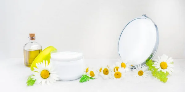 Herbal cosmetic body cream in opened container, bottle with natural oil, fresh chamomile flowers, mirror on white background. Natural organic moisturizer skincare. Selective focus. Wide banner mockup. — Stock Photo, Image