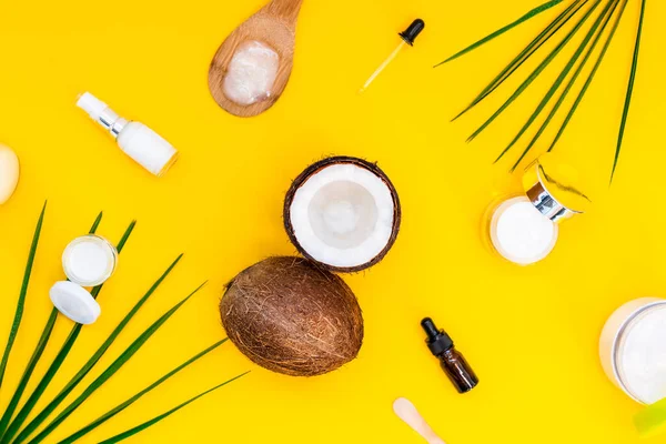 Top view biologische natuurlijke cosmetica voor gezichts- en lichaamsverzorging met kokosolie op gele achtergrond. Verse kokosnoten en verschillende room containers en essentiële olie flessen met palmbladeren. Plattegrond. — Stockfoto