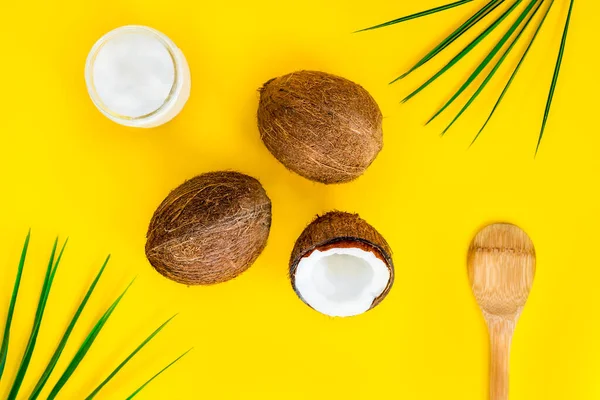 Bovenaanzicht biologische bio kokosboter met twee hele verse kokosnoten, de ene helft en palmbladeren op gele achtergrond. Natuurlijke olie voor koken en huidverzorging schoonheid. Plattegrond. — Stockfoto