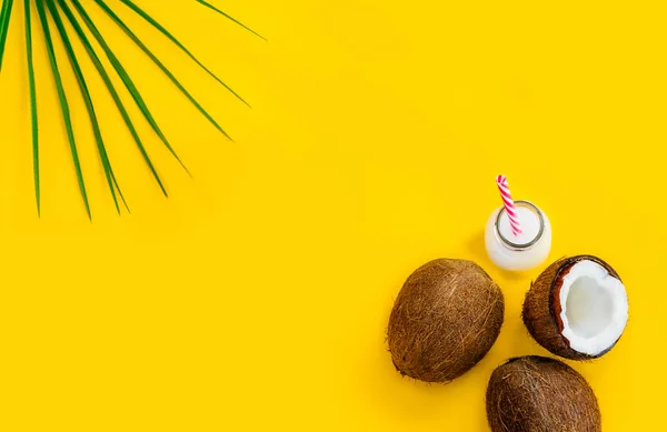 Bovenaanzicht kokoswater drinken, melk in een fles met stro, en verse kokosnoten met een groen palmblad op de gele achtergrond. Zomer exotische verfrissing. Natuurlijke plantaardige voedsel. Vlak leggen. Kopieerruimte. — Stockfoto