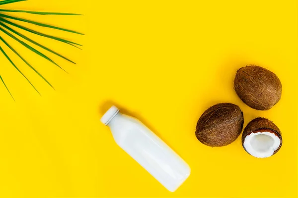 Bovenaanzicht fles verse rauwe veganistische kokosmelk en verse kokosnoten met een groen palmblad op de gele achtergrond. Zomer exotische verfrissing. Natuurlijke plantaardige voedsel. Kopieerruimte. — Stockfoto