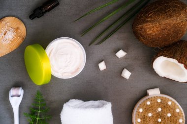 Vücut derisi için doğal kaplıca - Hindistan cevizi kozmetik ürünleri ve taze hindistan cevizi. Kremler, yağlar, deniz tuzu, masaj fırçası, koyu gri arka planda mezoroller. Sağlık ve refah. Düz Yatay.